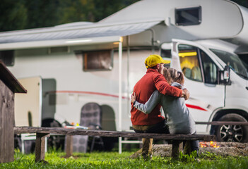 Father and His Daughter Enjoys a Cozy Evening by Their Camper Van on a Wooden Bench