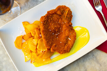 Appetizing crunchy breaded beef cutlet served with fried potato on white plate