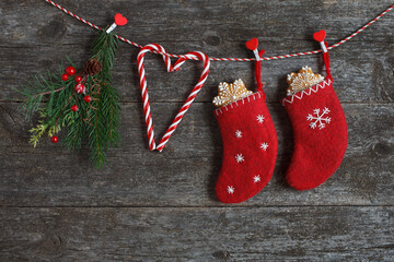 Christmas wooden background with red socks hanging on a rope, stockings with gifts, snowflake cookies, lollipop stick, fir branches. Postcard for congratulations