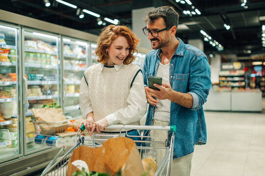 Couple using smartphone while shopping for groceries in supermarket