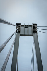 Naklejka premium Close-up view of the structural cables and metal pillars of a modern suspension bridge against a cloudy sky. The cables are tensioned, connecting the tall steel supports.