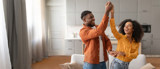 African American couple enjoys a moment of happiness as they dance together in a stylish living room. The warm atmosphere enhances their joyful expressions and lively interaction.