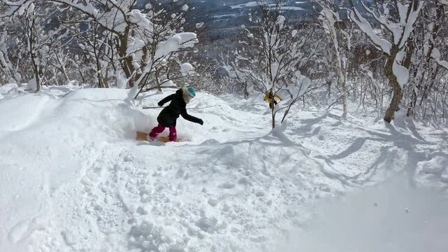 Two snowboarders riding through fresh powder snow in a bright, snowy forest. Snow sparkles under sunlight as they search for untouched lines down the mountain slope. White winter wonderland in Japan.