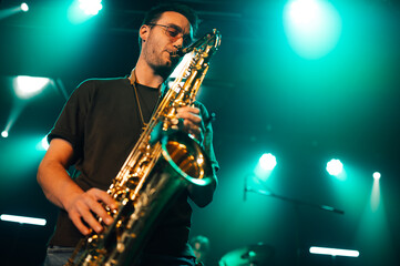 Saxophonist performing live on stage with teal lighting