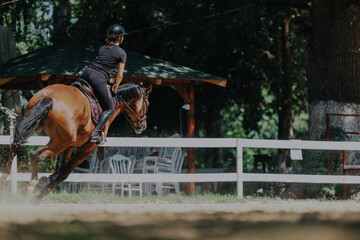 A young equestrian skillfully rides a horse in an outdoor arena, surrounded by lush greenery. The...