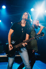 Fototapeta premium Guitarist and singer performing energetically on stage under blue lights