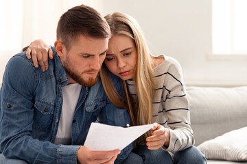 Calculating family budget. Upset couple reading financial statement from bank at home, empty space