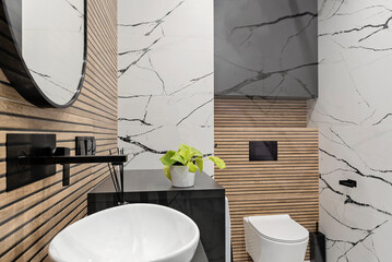 Modern interior of bathroom with ceramic wash basin with black faucet and brown striped tiles on the wall and circle mirror. Luxurious hygiene room in industrial style. Elegant home.