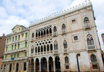 A view of historic Venetian buildings along the Grand Canal, showcasing classic Italian architecture. The iconic canal waters reflect the facades, with boats and gondolas adding to the charm of Venice