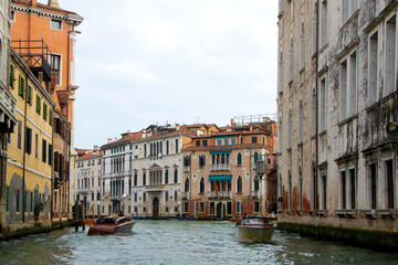 A view of historic Venetian buildings along the Grand Canal, showcasing classic Italian architecture. The iconic canal waters reflect the facades, with boats and gondolas adding to the charm of Venice