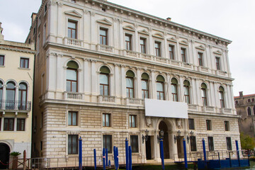 A view of historic Venetian buildings along the Grand Canal, showcasing classic Italian architecture. The iconic canal waters reflect the facades, with boats and gondolas adding to the charm of Venice