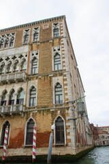 A view of historic Venetian buildings along the Grand Canal, showcasing classic Italian architecture. The iconic canal waters reflect the facades, with boats and gondolas adding to the charm of Venice