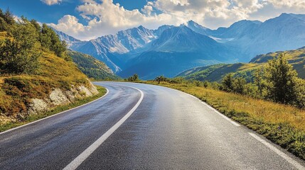 Fototapeta premium Winding mountain road curves through lush alpine landscape, leading towards majestic snow-capped peaks under a dramatic sky with billowing clouds.