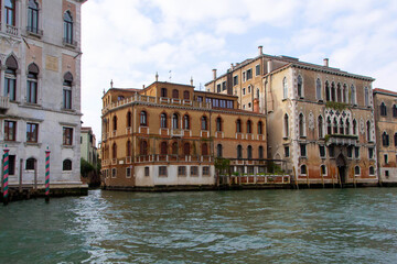 A view of historic Venetian buildings along the Grand Canal, showcasing classic Italian architecture. The iconic canal waters reflect the facades, with boats and gondolas adding to the charm of Venice