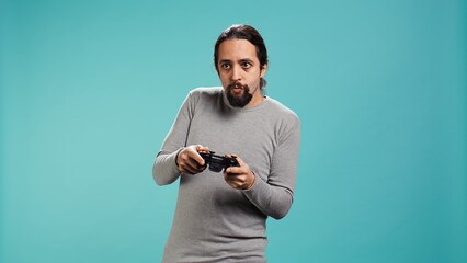 Fototapeta premium Upbeat person playing intense gaming console game, having fun, isolated over studio background. Joyous man pleased after being victorious in videogame, defeating all enemies using gamepad, camera B
