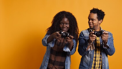 African american young woman making her husband lose the video game, feeling happy and celebrating her online gaming tournament win. Joyful relaxed married couple playing competition. Camera B.