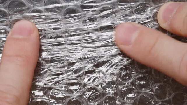 Macro shot of fingers pressing bubble wrap, emphasizing the act of popping bubbles as an anti-stress activity, with a focus on the texture and pressure applied by the hand.