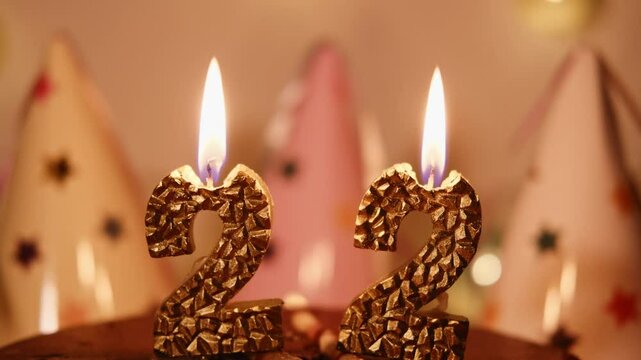 Number 22 year in golden candles shape in a chocolate cake. A homely atmosphere of a happy Birthday party. Garlands, paper caps and candle lights create comfort and warmth