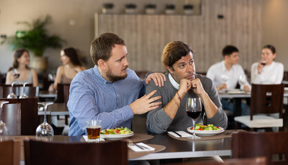 Two friends meeting in a modern restaurant - man comforts his upset sad friend
