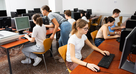 Fototapeta premium Interested young female student with glasses working on computer in university library, looking for necessary information on Internet