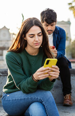 Naklejka premium Vertical shot of focused young woman using mobile phone sitting at city street, chatting online or reading some news on internet. Social media concept