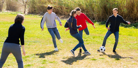 Cheerful teenagers are jogning with ball in spring park