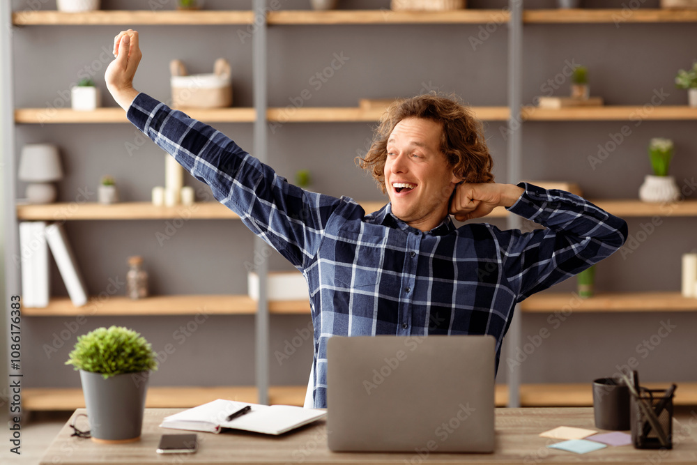 Poster funny freelancer guy at laptop stretching arms and yawning after work on computer sitting at desk in