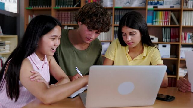 Three young multiracial group of high school students working together on laptop at library. Education and youth lifestyle concept.