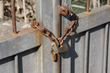 Iron gate locked by an old rusty padlock and a rusty chain