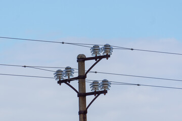 Old electric pole made out of concrete with wires and glass insulators against a blue hazy sky