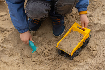 Child playing in a sandbox with a toy dump truck and plastic shovel. Outdoor activity, childhood creativity and imaginative play in a natural environment © Volha