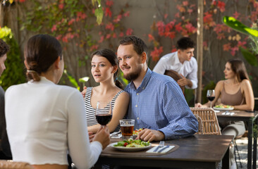 Two couples of men and women drinking eating and talking on restaurant terrace