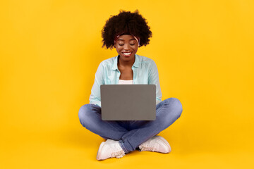 Cheerful African American Female Using Laptop Working Online And Browsing Internet Sitting On Pink Background. Black Female Typing Writing Article For Blog On Computer. E-Learning, Freelance And