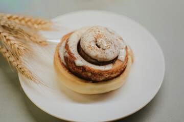 Fresh close-up cinnabon with butter cream on a plate on a gray background with wheat for cafe