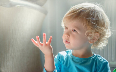 Sweet little child boy watching the dust particles in the morning light from the window