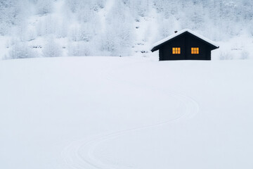 A small cabin is in the snow with a path leading to it
