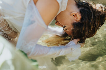 Image of a woman leaning over water, washing her hair, depicting a serene and tranquil moment in a natural setting.