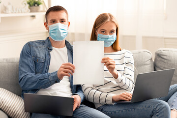 Work from home. Young couple working online on laptops and holding warning poster, covid-19 outbreak prevention