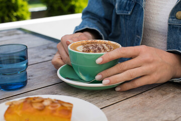 Woman holding cup with cappuccino at outdoor cafe table