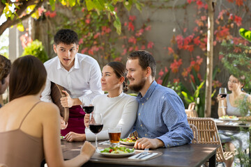 Young waiter talking to restaurant guests - taking orders for food and drinks