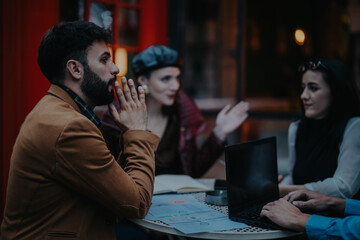 A group of business professionals engage in a serious discussion outdoors, with a focus on teamwork and collaboration. They are gathered around a table with a laptop and printed documents.