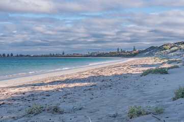 Warnbro Beach in Western Australia, featuring a pristine shoreline, gentle waves, and a vast horizon under a cloudy sky. A serene coastal landscape ideal for relaxation and nature appreciation.