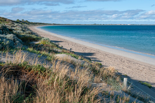 Warnbro Beach in Western Australia, featuring a pristine shoreline, gentle waves, and a vast horizon under a cloudy sky. A serene coastal landscape ideal for relaxation and nature appreciation.