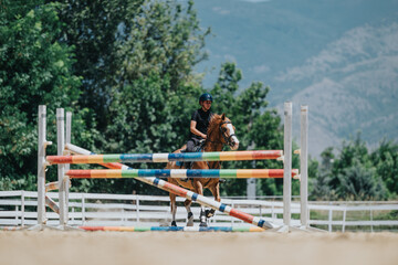 Fototapeta premium Equestrian rider demonstrating horse jumping skills in an outdoor arena. Scenic view with a focused rider and beautiful landscape.