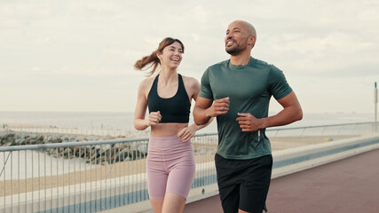 Close-up of young couple of athletes wearing sportswear running on the seafront outdoors