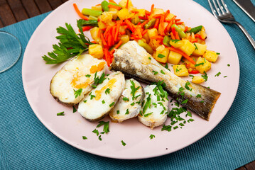 Closeup of sliced fried codfish served with potatoes and carrots at plate