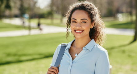 Naklejka premium Smiling young Latina woman in park, wearing light blue shirt, carrying backpack