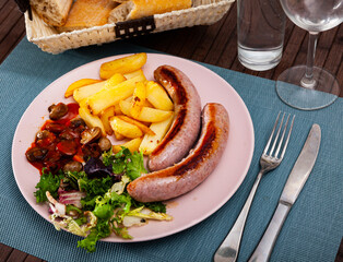 Fried homemade sausages with baked potatoes, mushrooms and lettuce at plate