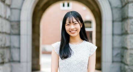 Fototapeta premium Asian woman smiling with straight hair in white attire standing under stone archway