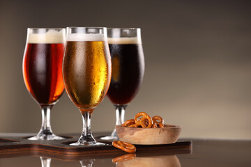 Glasses with different types of beer and snacks on mirror surface, closeup. Space for text